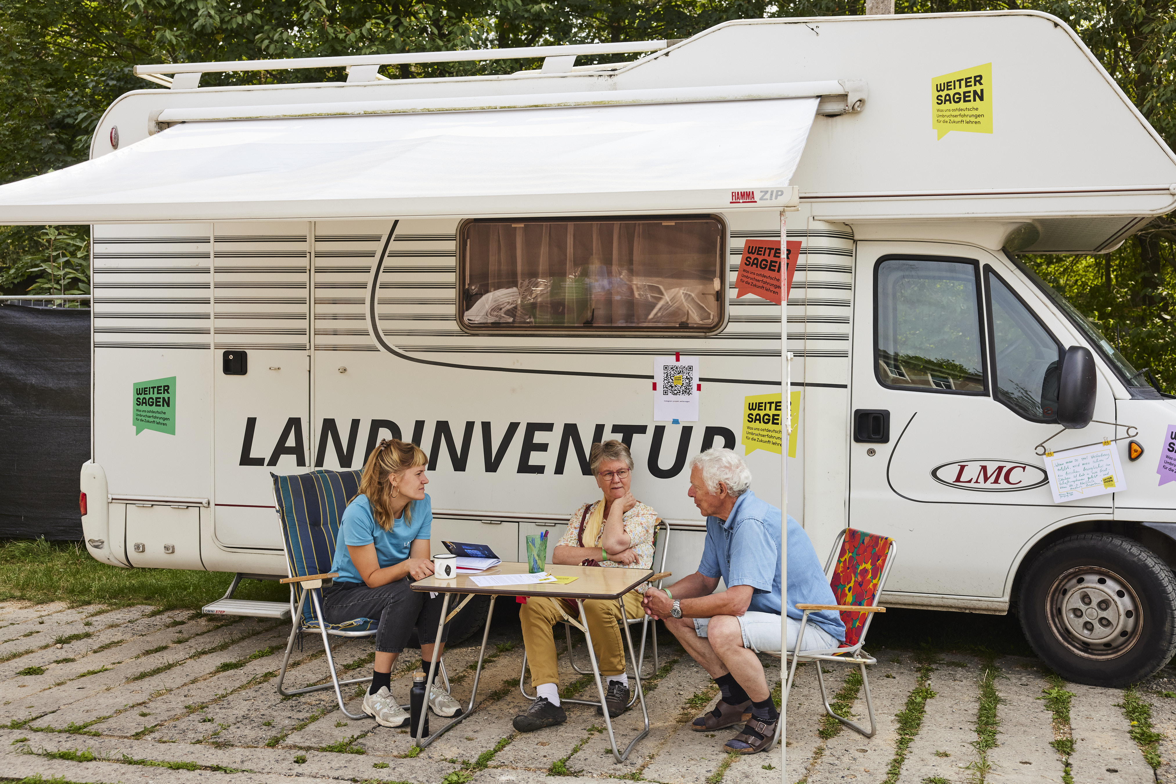 Menschen sitzen vor einem Wohnmobil und unterhalten sich