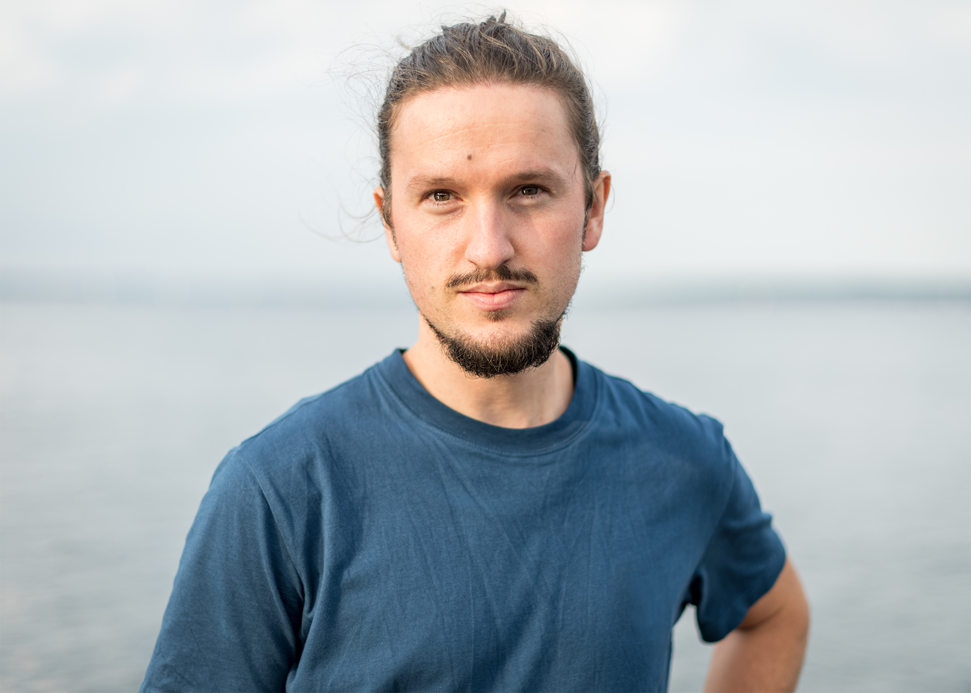 ein Mann im blauen T-Shirt steht vor dem Meer