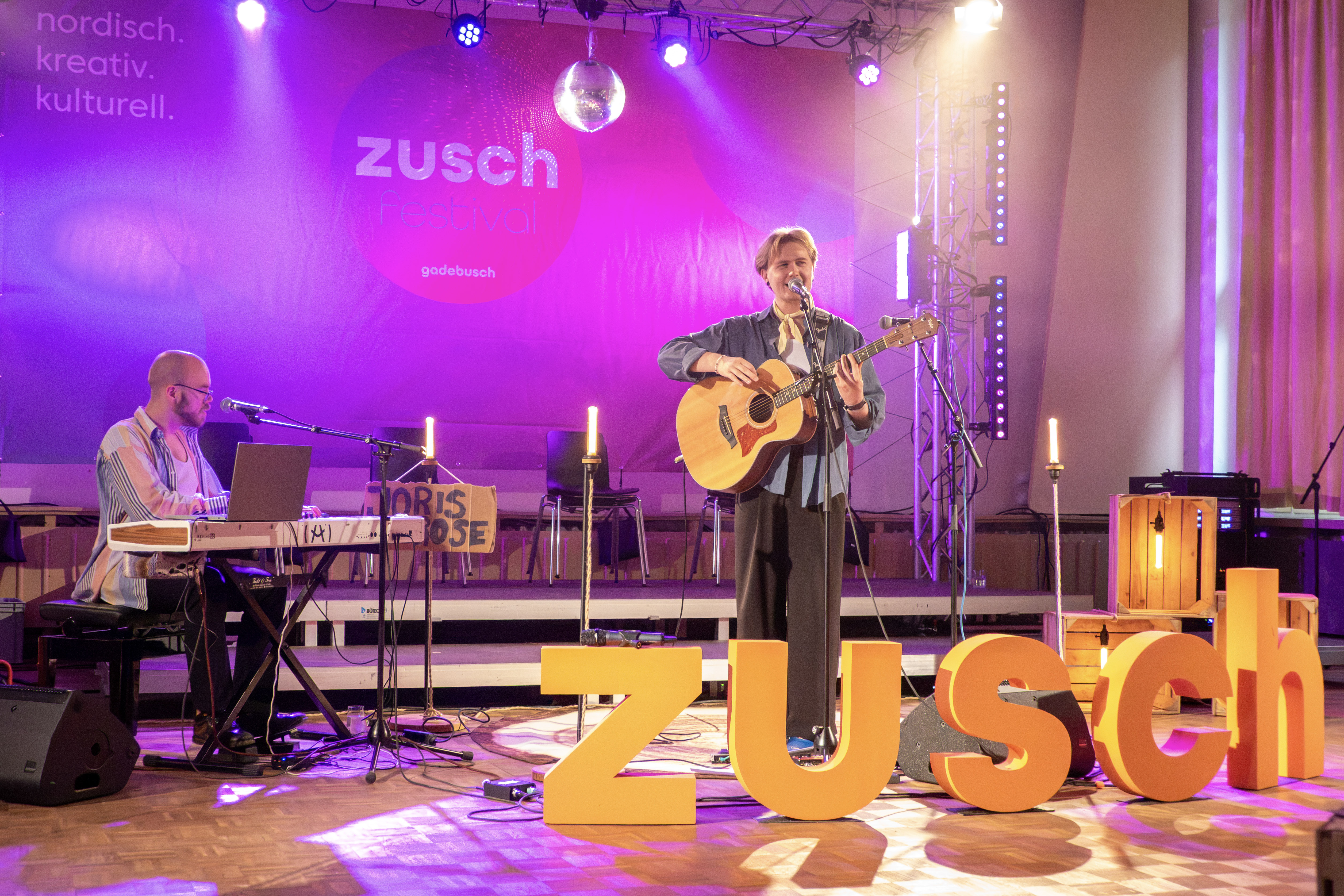 ein Sänger mit Gitarre singt und wird von einem Pianisten begleitet