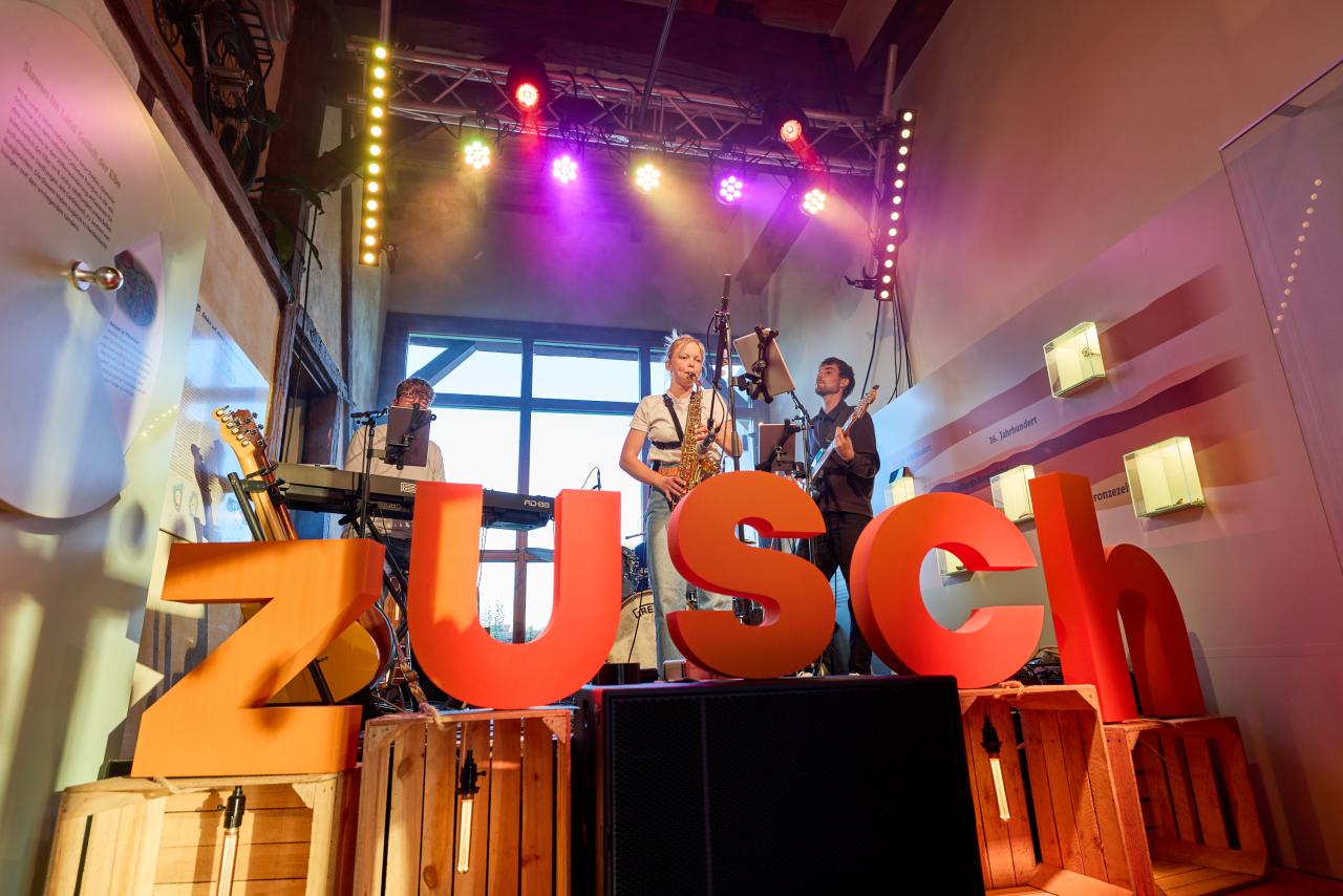© Oliver Borchert Eine Band steht auf der Bühne hinter den Buchstaben "zusch"