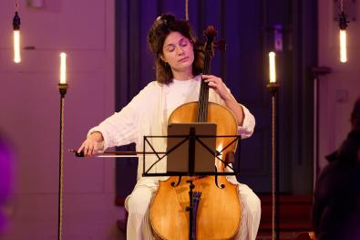 Eine Cellistin sitz zwischen Lampen und spielt mit geschlossenen Augen Cello