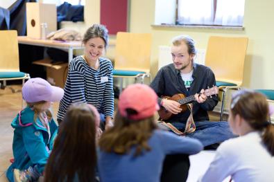 Eine Musikerin und ein Musiker mit Gitarre sitzen mit Kindern im Kreis