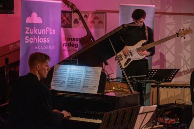 Mann spielt am Klavier, Gitarrist im Hintergrund